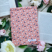 Flat Lay of Eliza placed on some open books. Some pink and yellow flowers are also in the picture.